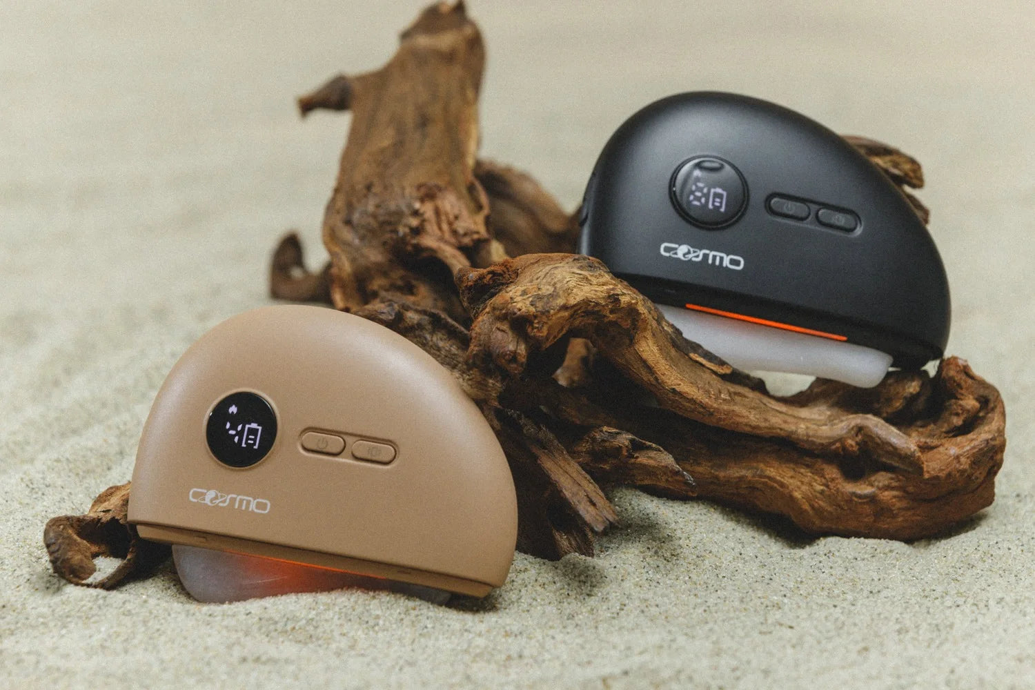 Gua sha at home facial tools in black and beige resting on driftwood and sand with glowing red light therapy.