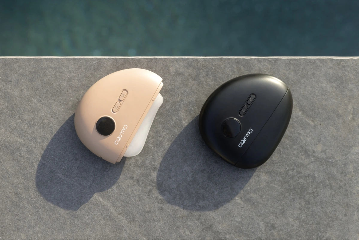 Electric gua sha tools in beige and black placed side by side on stone surface near water in natural light.