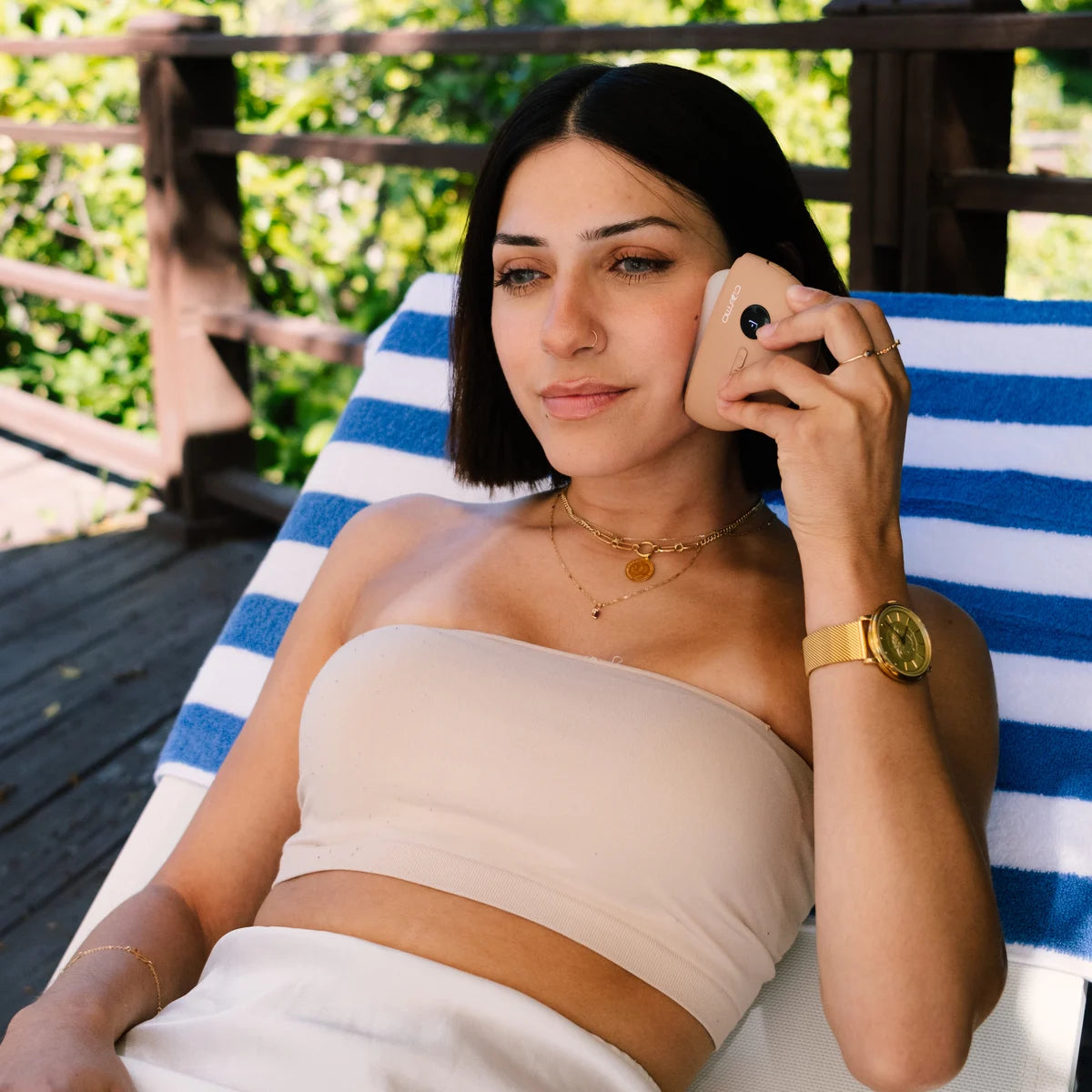 Gua sha face tool used by woman reclining on lounge chair outdoors, gently massaging her cheek in the sun.