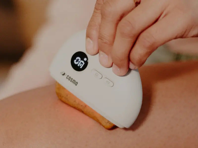 At-home gua sha tool applied to the leg with visible LED screen and ergonomic handheld design