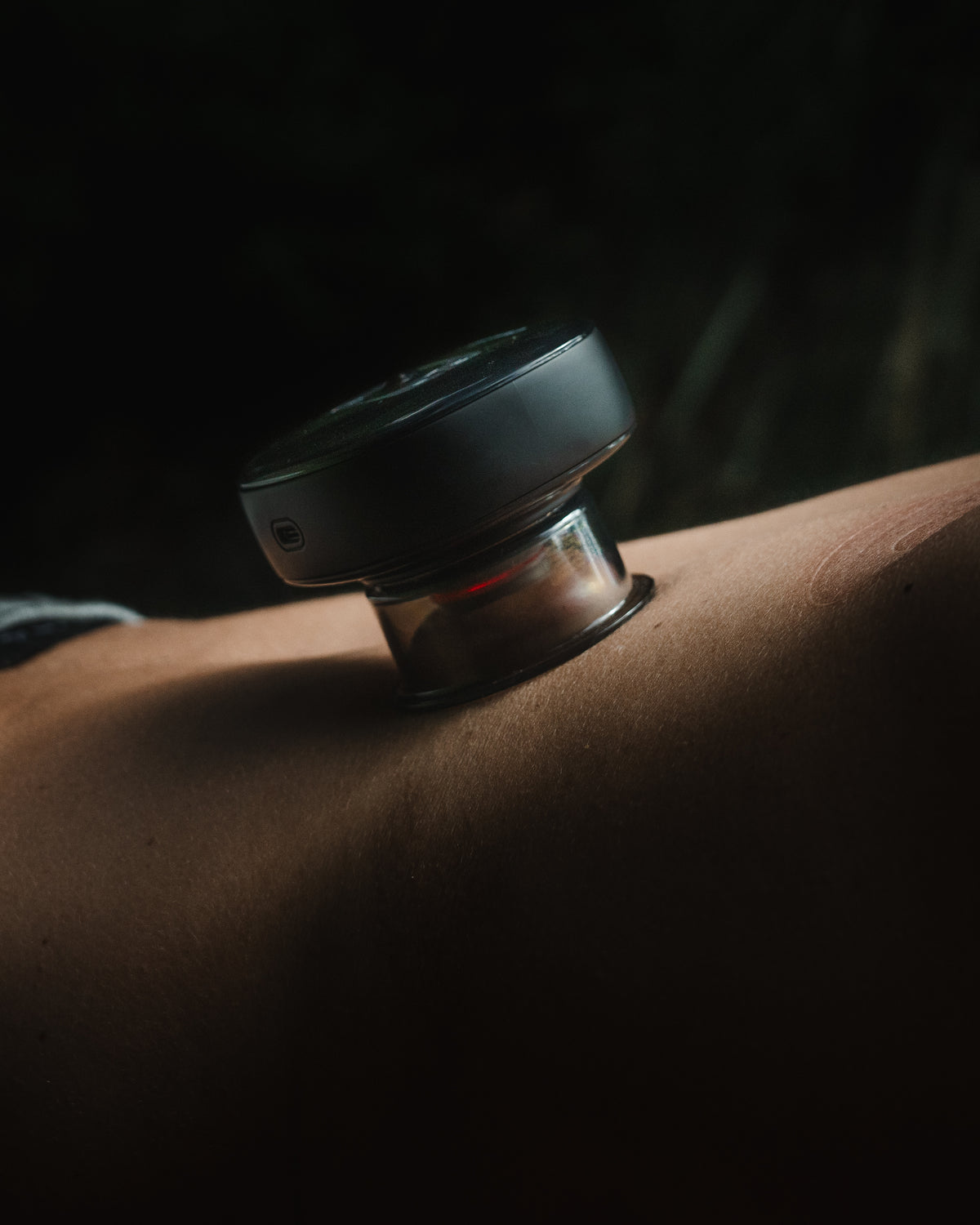 Smart cupping device with red light therapy applied to bare skin during a massage session in a dark setting.