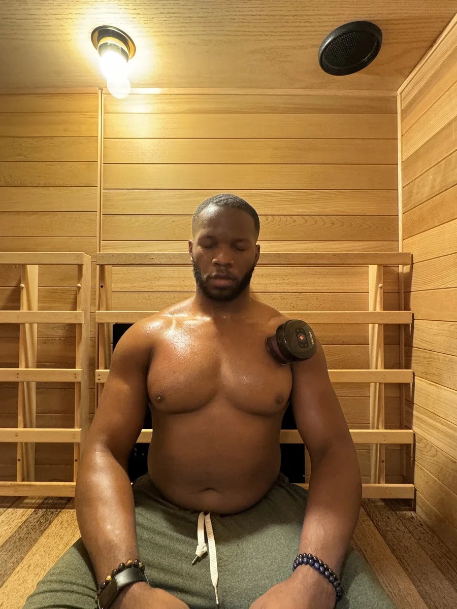 Portable cupping device in use on man's shoulder as he relaxes shirtless in a wooden sauna.