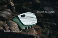 Roller jade for face device resting on natural rocks with sunlight highlighting its sleek, modern design and jade base.