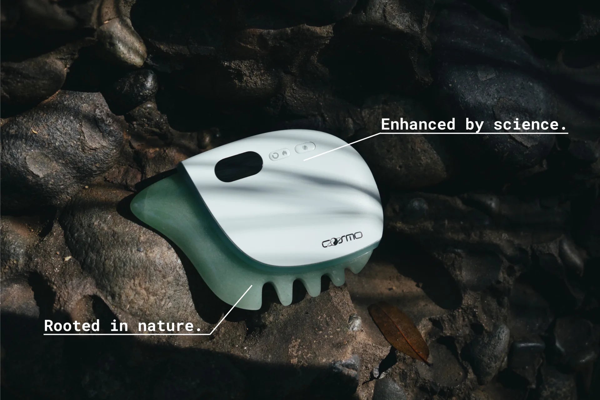 Roller jade for face device resting on natural rocks with sunlight highlighting its sleek, modern design and jade base.