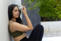 Jade stone face roller used by woman relaxing outdoors with eyes closed and pressing it gently to her forehead.