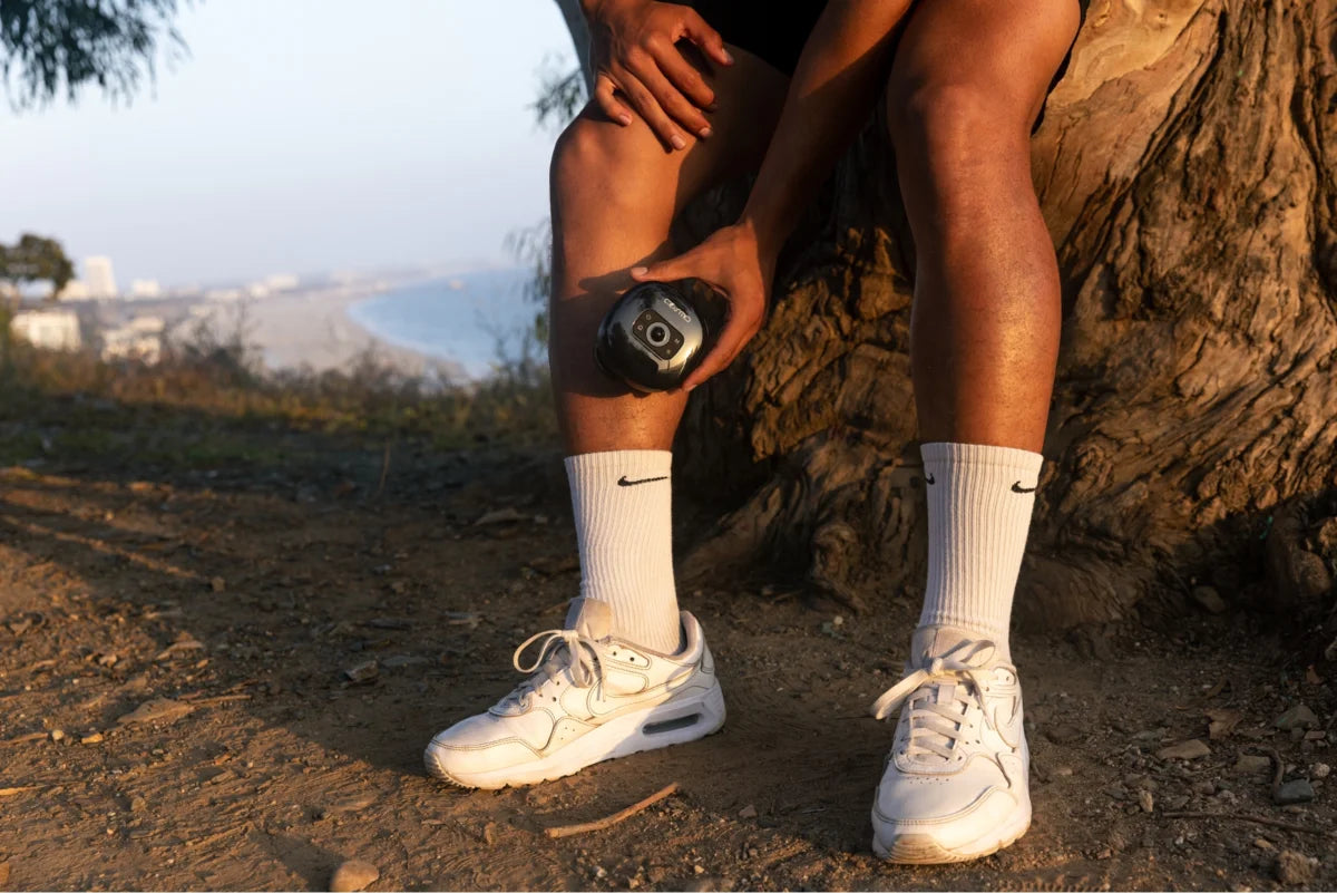 Portable cupping device used on lower leg by man resting outdoors near beach at sunset with athletic gear.